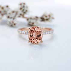 a ring with an oval cut peach morganite surrounded by white diamonds on a table