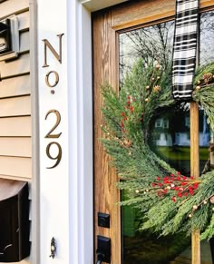 a wreath is hanging on the front door of a house that has been decorated with evergreen and red berries