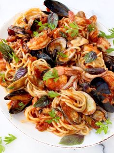 pasta with clams, shrimp and tomato sauce on a white plate topped with parsley