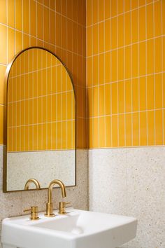 a white sink sitting under a bathroom mirror next to a yellow tiled wall with gold faucets