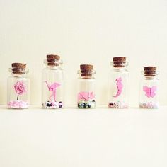 five glass bottles with pink flowers and butterflies in them