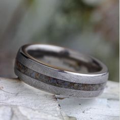 two wedding bands made out of silver and brown wood are sitting on top of a rock