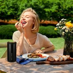 a woman sitting at a table with food and drinks in front of her, while talking on the phone