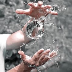 two hands are holding an object in the air with water splashing on them and one hand is reaching out to it