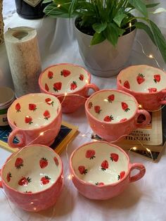 four pink cups with red flowers on them sitting on a table next to some books