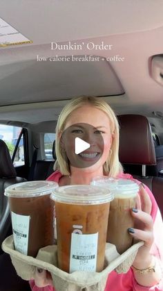 a woman holding two cups of coffee in her car