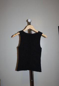 a black sweater vest hanging on a wooden hanger in front of a white wall