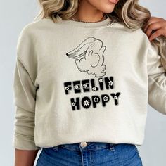 This cozy Easter sweatshirt is the perfect addition to your holiday wardrobe! Featuring an adorable bunny design, the playful graphic is made even more fun with floral font accents. The soft and comfortable material ensures that you'll want to wear it all season long. Whether you're dressing up for a family gathering or lounging at home, this cute and stylish sweatshirt is sure to be a hit. Order now and hop into the Easter spirit! NOTE: Design is for Womens sweatshirt or Childrens Tshirt.  Plea Casual Winter Tops With Cartoon Print, Winter Cartoon Print Tops For Loungewear, Trendy Winter Tops With Cartoon Print, Cute Winter T-shirt For Loungewear, Winter Cartoon Print Relaxed Fit Tops, Winter Fun Relaxed Fit Tops, Cozy White Graphic Print T-shirt, Fun Winter Tops With Relaxed Fit, Playful Relaxed Fit Winter Tops