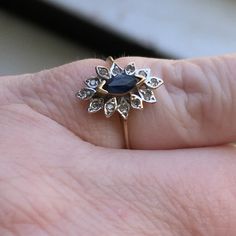 a woman's hand holding a ring with a blue stone in it and diamond accents