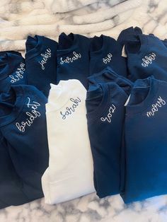 six blue and white onesuits with names on them sitting on a bed together