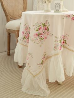 a white table with pink flowers on it next to a chair and clock in the corner