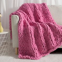 a pink knitted blanket sitting on top of a couch next to a white table