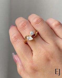 a woman's hand wearing a gold ring with two pear shaped diamonds on it