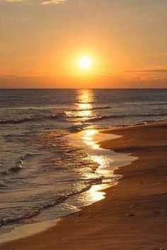 the sun is setting over the water on the beach