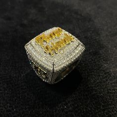 a yellow and white diamond ring sitting on top of a black surface with the word love spelled in gold letters