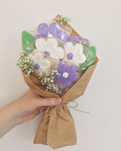 a hand holding a bouquet of flowers wrapped in brown paper with purple and white buttons