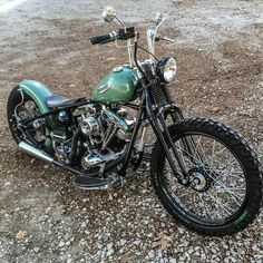 a green motorcycle parked on top of a gravel field