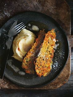 two pieces of food on a black plate with a fork and knife next to it