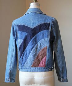 a blue jean jacket with multicolored waves on the front and back, sitting on a mannequin head