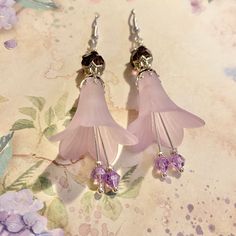 Ethereal Purple Fairy Flower Earrings These delicate earrings capture the essence of a magical fairy realm. A soft purple flower, crafted from lucite blooms with ethereal beauty. The petals are adorned with tiny amethyst glass crystals that shimmer like stardust. The earrings are suspended from silver 925 ear wires, completing the enchanting design. Wear these earrings as a reminder of the enchanting allure found in everyday moments and let your inner fairy shine through. Add a sprinkle of charm Tiny Crystal Earrings, Lavender Bridesmaids, Pansy Earrings, Lilac Fairy, Fairy Realm, Lavender Bridesmaid, Purple Fairy, Fairy Earrings, Silver Fairy