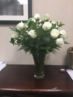 a vase filled with white roses sitting on top of a wooden table next to a wall