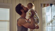 a man holding a baby in his arms and kissing it's face with the other hand