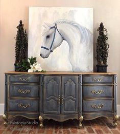 a painting of a white horse is on the wall above an antique dresser with flowers and potted plants