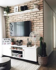 a living room with brick wall and white entertainment center, plants on top of it