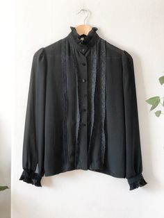 Vintage 60s black sheer secretary blouse. Features six button closures, button wrists, ruffle hem neck and sleeves, lace details up front and slightly puffed sleeves. A classic blouse for a classy someone.  Label: Style Rite Blouse Co. - Toronto Fits Like: women's small Color: black Fabrication: chiffon / polyester Condition: good vintage condition, normal signs of wear 14.5" shoulder 37" chest 35" waist 24" sleeve 24" length This item comes from a pet & smoke free building. For a look behind the scenes at our treasure hunting trips follow us at: + Instagram: @mostlymagicvintage + TikTok: @mostlymagik Retro Black Button-up Blouse, Formal Fitted Blouse With Ruffled Collar, Elegant Blouse With Peter Pan Collar And Buttons, Black Ruffled Button-up Blouse, Elegant Tops With Peter Pan Collar And Buttons, Long Sleeve Office Blouse With Lace Trim, Fitted Blouse With Lace Collar For Office, Long Sleeve Blouse With Lace Trim For Office, Black Lace Cuffs Blouse For Fall