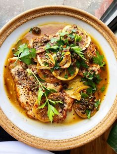 a white plate topped with fish covered in olives and herbs on top of a window sill