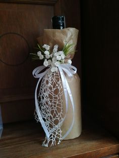 a brown paper bag with white flowers and ribbon tied around it sitting on a wooden shelf