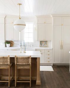 a kitchen with white cabinets and wooden chairs in front of an island countertop that has two stools on it