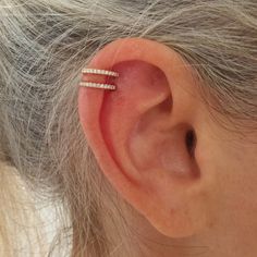 an older woman's ear with two thin white diamond barbells on it