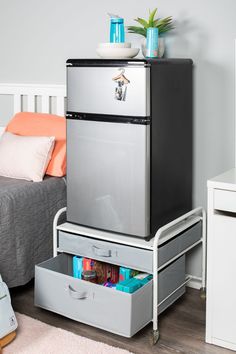 a silver refrigerator freezer sitting on top of a metal drawer next to a bed