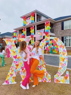 two girls standing in front of a large letter decorated with balloons