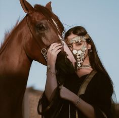 a woman in black dress standing next to a horse with gold jewelry on it's face