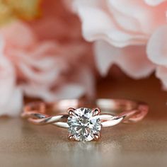 a close up of a diamond ring on a table with flowers in the back ground