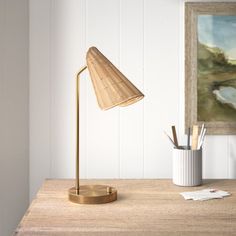 a desk lamp sitting on top of a wooden table next to a painting and pencils