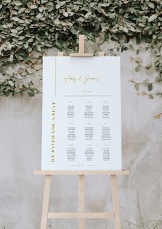 an easel stands in front of a wall with greenery and seating chart on it