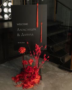 a welcome sign with red flowers in the foreground and a black background behind it