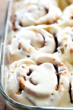 a pan filled with cinnamon rolls covered in icing on top of a wooden table