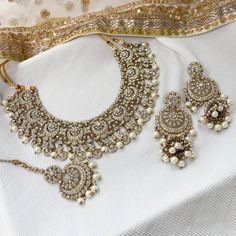 Beautifully flexible Antique Gold intricate necklace set scattered with dazzling clear rhinestone crystals and off white pearl bead detailing Comes with matching long jhumka earrings (approx 3 inch length x 1.5 inch width) and matching tikka ( pendant part 2 inch length x 1 inch width)  Ready to ship as seen with gift box! Traditional Crystal Bridal Sets For Festive Occasions, Silver Pearl Jewelry Set With Meenakari, Silver Pearl Jewelry Set With Meenakari Detail, Silver Meenakari Pearl Jewelry Sets, Silver Meenakari Jewelry Sets With Pearls, Traditional Crystal Jewelry Sets For Wedding, Festive Crystal Jewelry Sets With Stone Work, Silver Kundan Pearl Necklace With Stone Work, Bollywood Silver Jewelry Sets With Pearl Drop