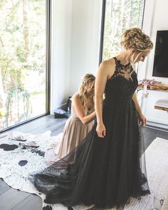 two women standing in front of a window looking at something on the floor while wearing dresses