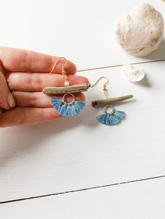 a pair of blue tasseled earrings on a white table next to seashells