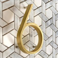 the number six in gold is displayed on a white wall with hexagonal tiles