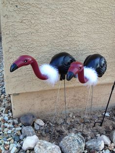 three flamingos are standing on top of each other in front of a building with rocks and gravel