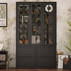 a black china cabinet sitting next to a wall with pictures on it and plants in the corner