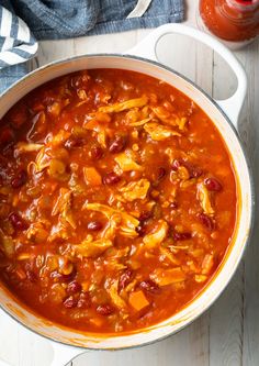 a pot filled with chili and chicken on top of a wooden table next to a jar of sauce