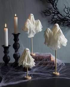 three halloween decorations with ghost heads on them and two candles in front of the table