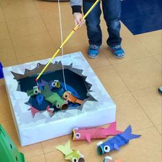 a child is playing with some construction paper and plastic fish in an ice block box